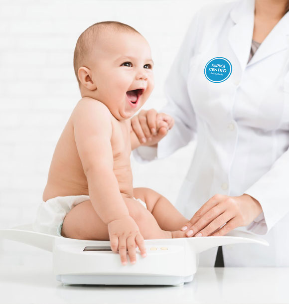 Un bebe siendo pesado en una bascula por una farmaceutica